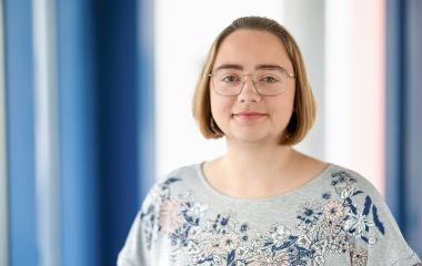 Eine Frau steht vor einem Fenster. Es ist die Bibliotheksmitarbeiterin Nadja Kerntopf.