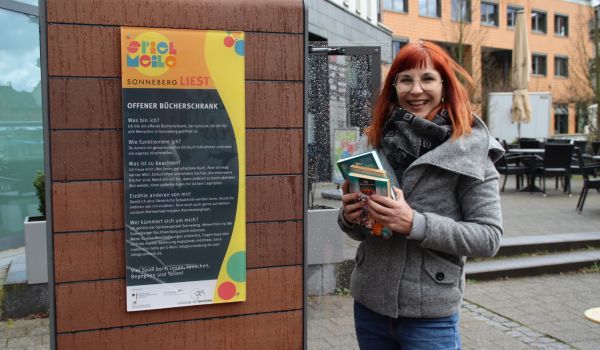 Frau mit Büchern vor dem Bücherschrank.