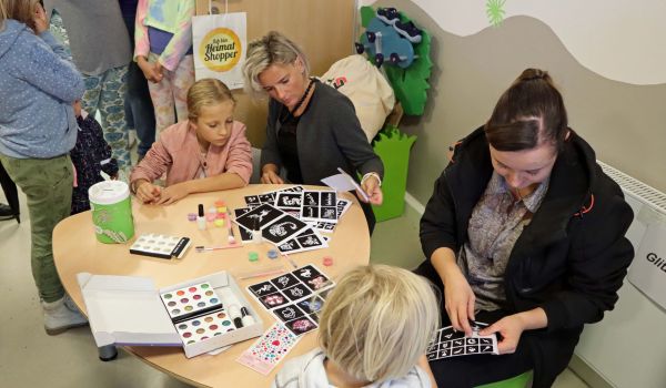 Kinder sitzen mit zwei Frauen an einem Tisch und basteln.