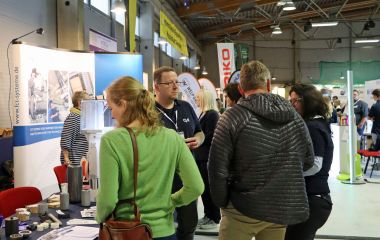 Menschen stehen vor einem Messestand und unterhalten sich.