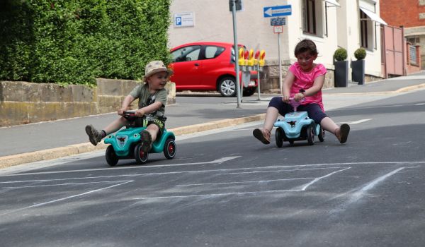 Zwei Kinder fahren auf Bobby-Cars die Straße herunter.