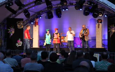 Fünf Personen treten auf einer Bühne auf. Einer von ihn spielt Gitarre.