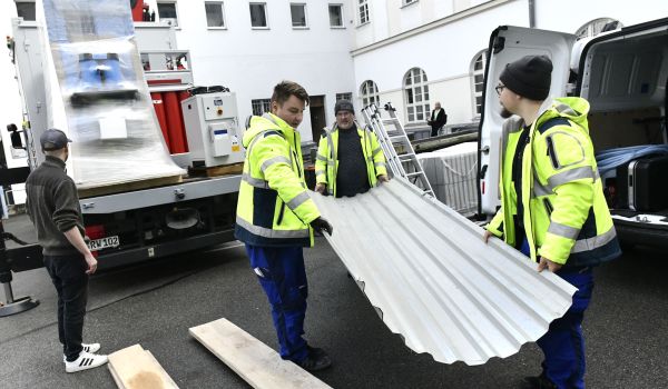 Männer in Warnjacken verladen ein Wellblech.