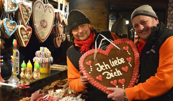 Zwei Männer halten ein ein Lebkuchenherz mit der Aufschrift: Ich liebe dich.