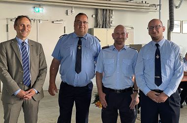 Drei Feuerwehrmänner in Uniform stehen nebeneinander. Links davon steht ein Mann im Anzug. Es ist der Hauptamtliche Beigeordnete Christian Dressel.