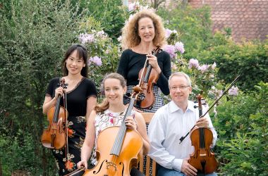 Vier Musiker mit Violinen, Violas und Cellos sitzen in einem Garten.