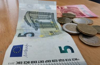 Ein Fünfeuroschein, ein Zehneuroschein und Kleingeld liegt auf einem Tisch.
