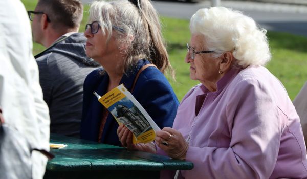 Eine Frau sitzt an einem Tisch im Freien. Sie hält ein Programmheft mit der Aufschrift: 30. Sonneberger Stadt- und Museumsfest, in den Händen.
