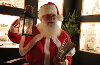 Ein Weihnachtsmann hält eine Laterne und ein goldenes Buch in den Händen.