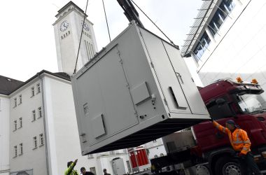 Ein großer weißer Container wird mit einem Kran verladen.
