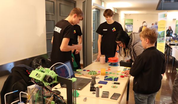 Jugendliche an einem Stand mit 3-D-Druckteilen.