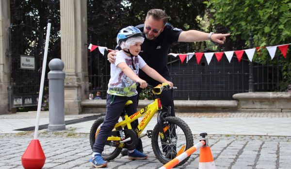 Ein Mann in Polizeiuniform zeigt einem Kind die Richtung. Das Kind trägt einen Helm und sitzt auf einem Fahrrad.