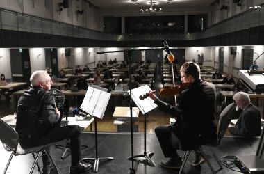 Ein Mann mit Akkordeon und ein Mann mit Geige sitzen auf einer Bühne und spielen.