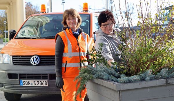 Zwei Frauen stecken Tannenzweige in einen Pflanzkübel.