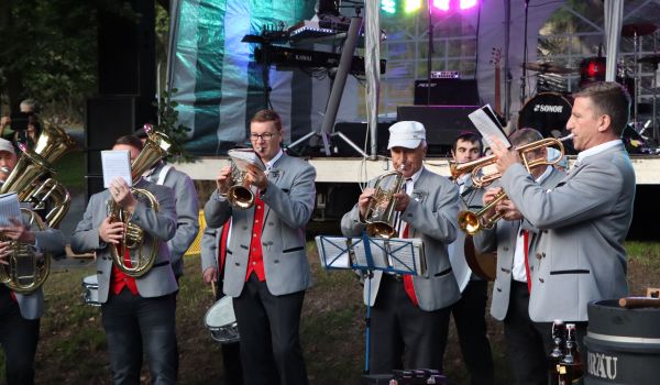 Männer in Tracht stehen vor einer Bühne und spielen Blechblasinstrumente.