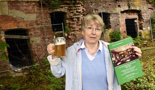 Eine Frau hält einen Krug mit Bier und ein grünes Buch in den Händen.