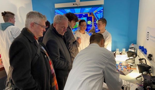 Ein Jugendlicher in weißem Kittel erklärt Experimente an Interessierte.