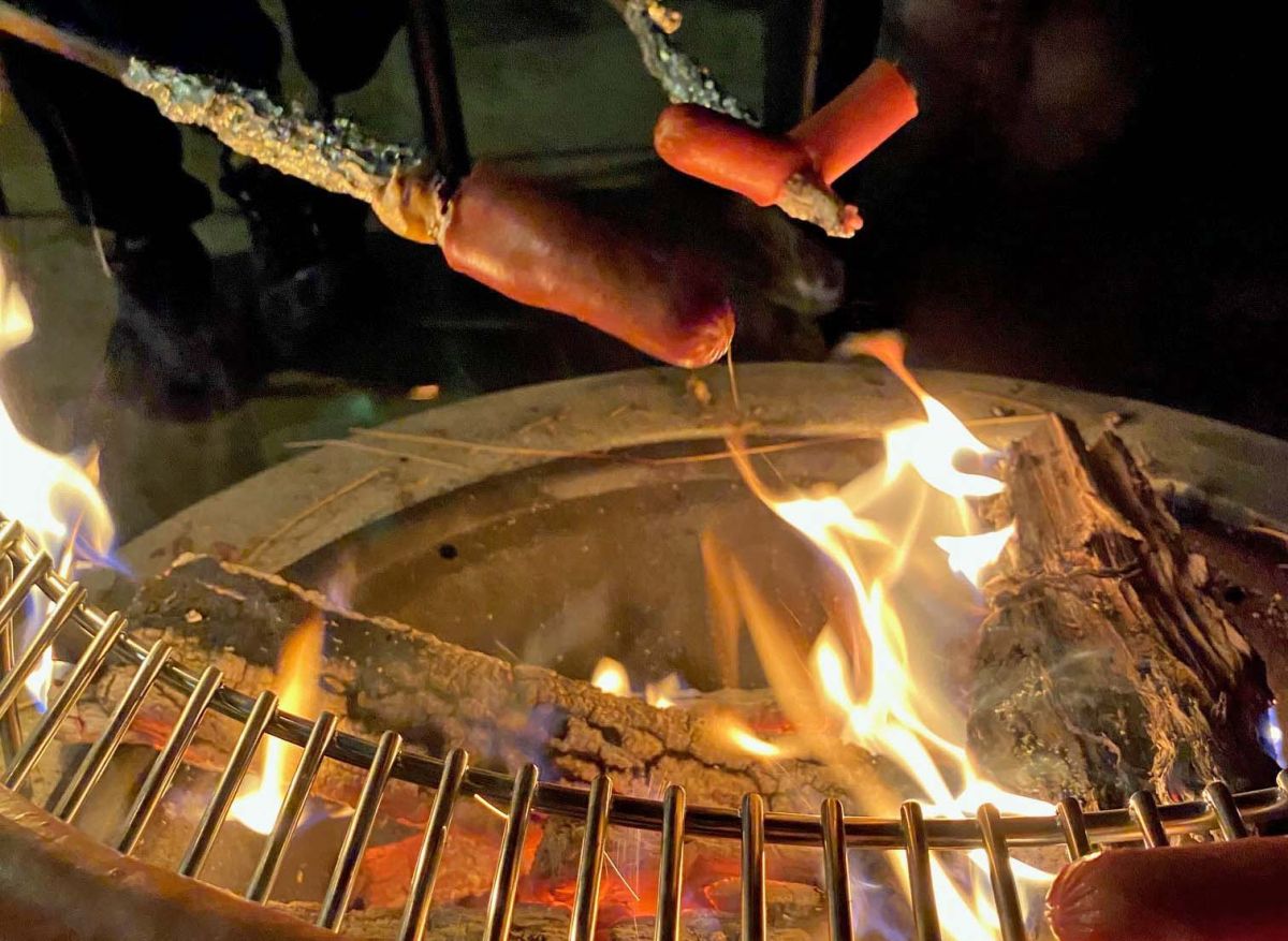 Zwei Stöcker mit Würstchen über einer Feuerschale.