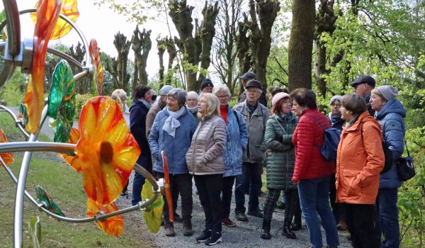 Eine Gruppe von Senioren steht auf einem Kiesweg vor einer Baumallee.