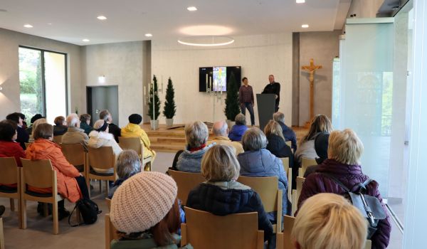 Eine Gruppe von Senioren sitzt auf Stühlen in einem Raum. Dieser wird für Trauerfeiern benutzt.