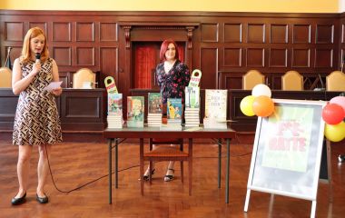 Eine Frau steht neben einem Tisch mit Büchern und spricht in ein Mikrofon.