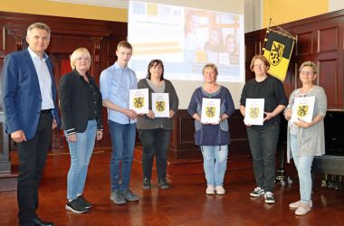 Sieben Personen stehen in einer Reihe. Links steht ein Mann in Anzug. Es ist der Bürgermeister Dr. Heiko Voigt. Fünf der Personen halten eine Urkunde in der Hand. Das Wappen der Stadt Sonneberg ist darauf.