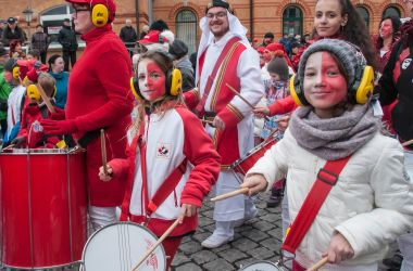 Rot weiß kostümierte Menschen ziehen trommelnd durch die Stadt.