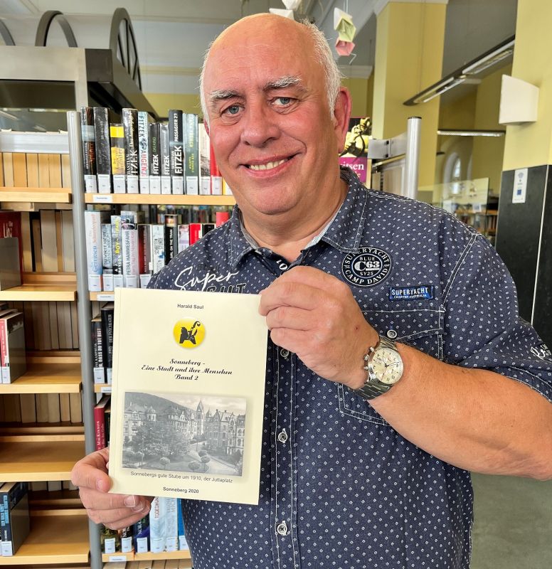Ein Mann hält ein Buch in der Hand. Im Hintergrund sind Bücherregale.