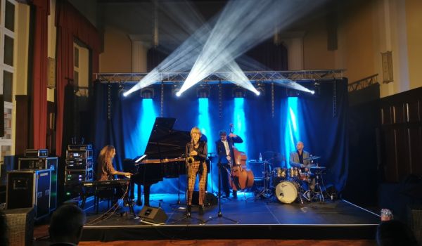 Eine Band tritt auf einer Bühne auf. Es ist dunkel. Bunte Scheinwerfer erhellen das Bild.