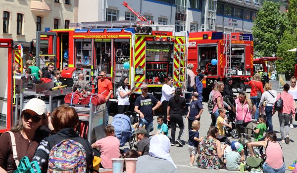 Feuerwehrautos stehen in der Innenstadt. Daneben stehen und sitzen Menschen.
