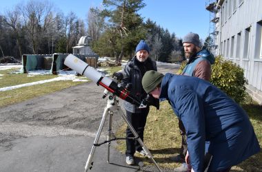 Ein Mann schaut durch ein Teleskop in den Himmel. Es scheint die Sonne.