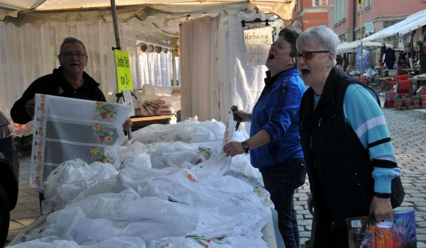 Ein Mann verkauft an einem Stand Gardinen. Vor dem Stand stehen zwei Kundinnen.