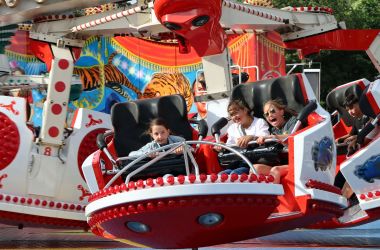Ein rotes Karussell mit lachenden Kindern auf einem Rummel.