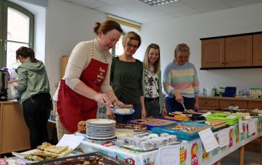 Vier Frauen stehen hinter einem Tisch. Auf dem Tisch stehen verschiedene Kuchen.