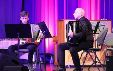 Zwei Personen sitzen auf einer Bühne und spielen Akkordeon.