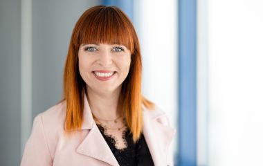 Eine Frau steht vor einem Fenster. Es ist Christiane Heim vom Stadtmarketing.