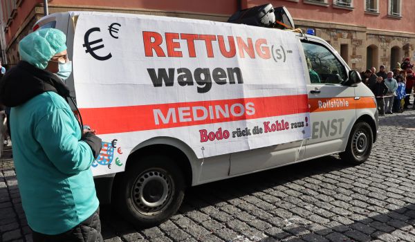 Personen laufen neben einem Rettungswagen. Sie sind als Chirurgen gekleidet.