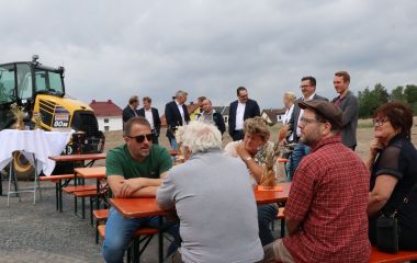 Menschen sitzen an auf Bierzeltgarnituren auf einer Baustelle.