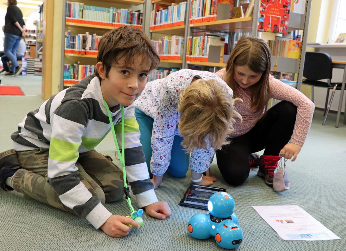Kinder, am Boden sitzen, beim Ausprobieren eines Programmierroboters, Foto: K. Zitzmann