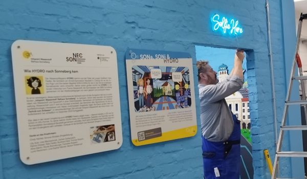 Ein Mann bringt ein Lichtzeichen an eine blaue Wand an.