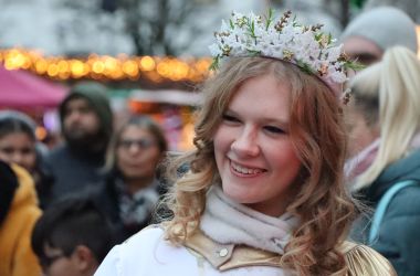 Eine junge Frau ist als Christkind gekleidet. Im Hintergrund stehen Menschen.