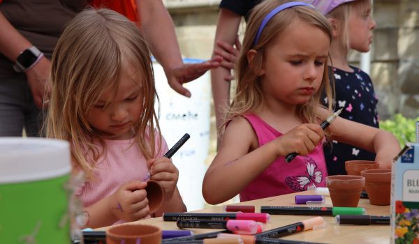 Kinder sitzen an einem Tisch und malen Blumentöpfe an.