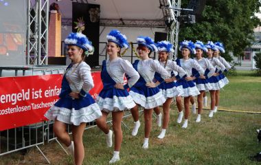Tanzmariechen tanzen vor einer Bühne entlang.