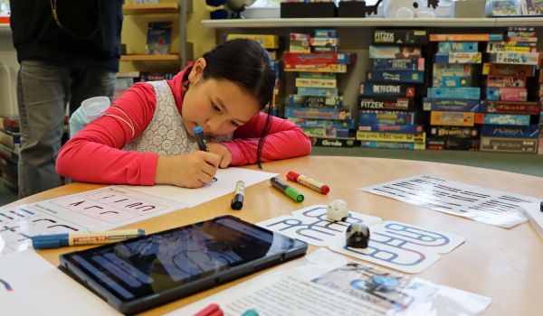 Ein Mädchen sitzt an einem Tisch und experimentiert mit einem Roboter.