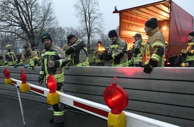 Feuerwehrmänner stellen eine Absperrung zum Schutz vor Hochwasser auf einer Straße auf.