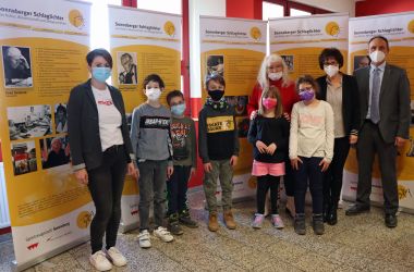 Eine Gruppe von Menschen steht vor veschiedenen Bannern in einer Schule.