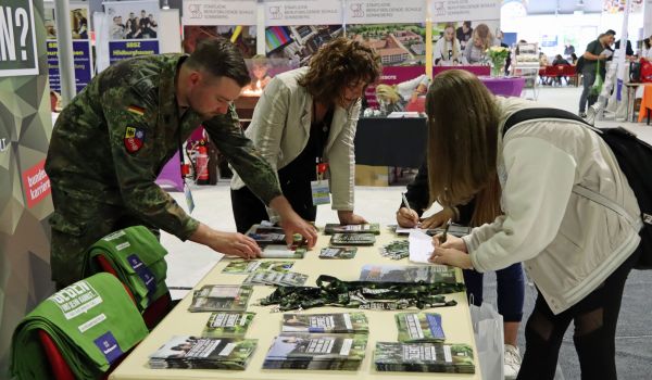 Vier Personen beugen sich über einen Tisch. Ein Mann trägt eine Uniform der Bundeswehr. Auf dem Tisch liegen Werbe-Flyer der Bundeswehr.