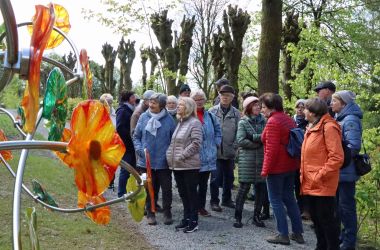 Eine Gruppe von Senioren steht auf einem Kiesweg vor einer Baumallee.