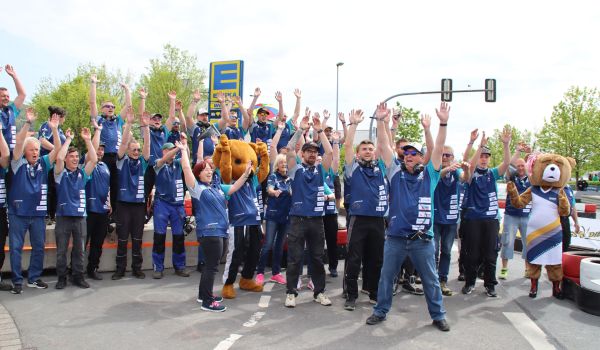 Menschen in blauen Trikots stehen nebeneinander und jubeln.