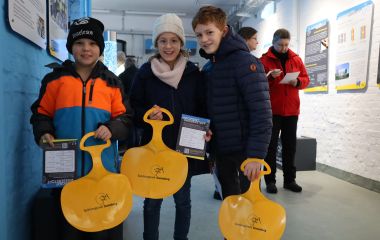 Kinder halten einen gelben Schneerutscher mit der Aufschrift: Spielzeugstadt Sonneberg, in den Händen.